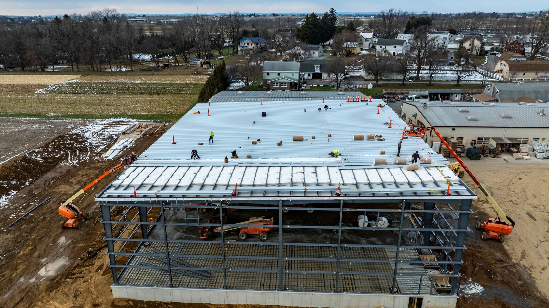 Construction Progress on a Large Building With Workers on Roof in Rural Area During Winter