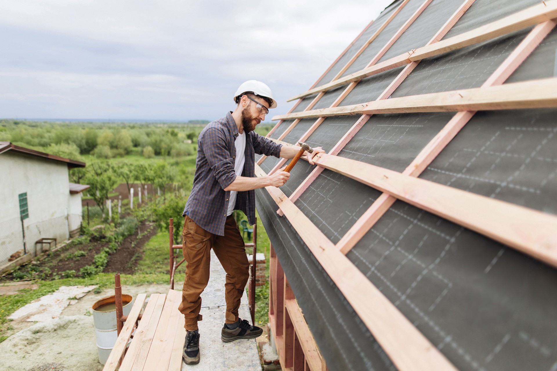 A man hammers nails into the rafters on the roof of a house